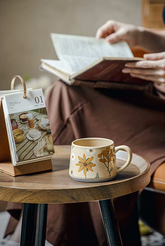Person Reading A Book With Enchanting Botanicals Pottery Mug Daisy Ceramic Cup On Table